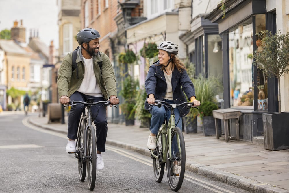 Two people cycling past some shops
