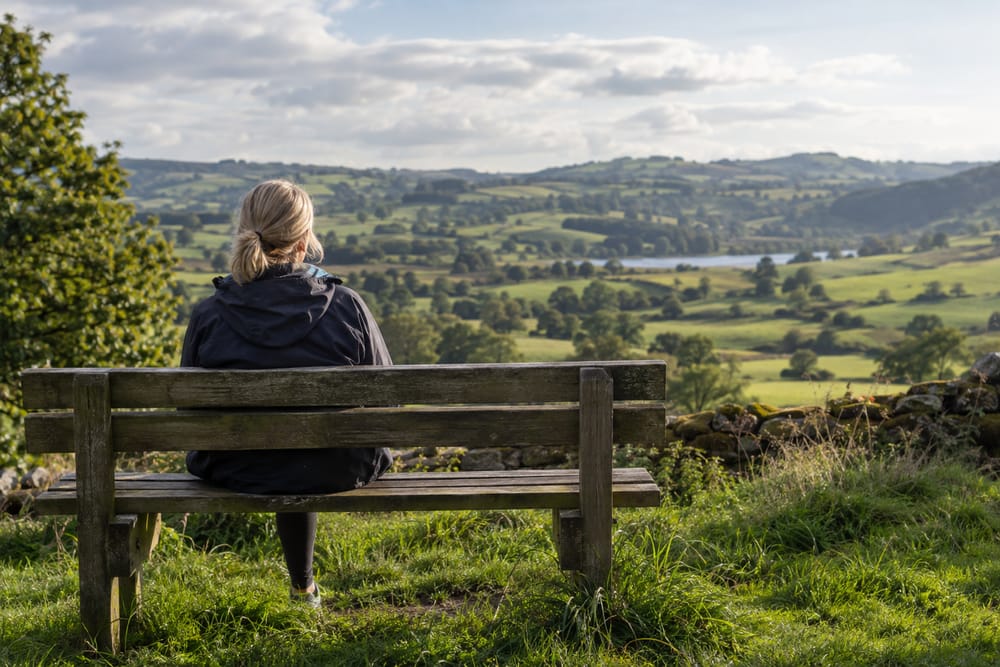 Woman sitting on a bench looking out over green countryside